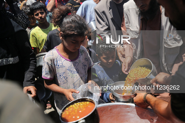 Displaced Palestinians are receiving food portions from a large pot at a public kitchen in Deir el-Balah in the central Gaza Strip on May 13...