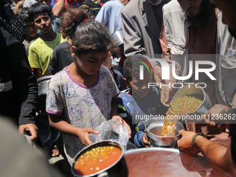 Displaced Palestinians are receiving food portions from a large pot at a public kitchen in Deir el-Balah in the central Gaza Strip on May 13...