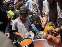 Displaced Palestinians are receiving food portions from a large pot at a public kitchen in Deir el-Balah in the central Gaza Strip on May 13...