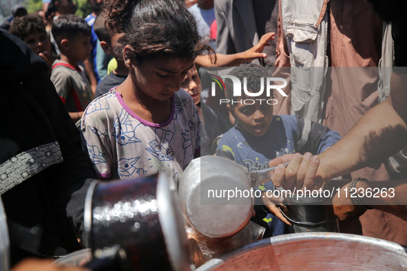 Displaced Palestinians are receiving food portions from a large pot at a public kitchen in Deir el-Balah in the central Gaza Strip on May 13...