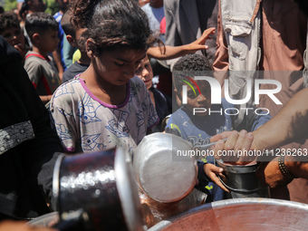 Displaced Palestinians are receiving food portions from a large pot at a public kitchen in Deir el-Balah in the central Gaza Strip on May 13...