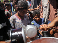 Displaced Palestinians are receiving food portions from a large pot at a public kitchen in Deir el-Balah in the central Gaza Strip on May 13...