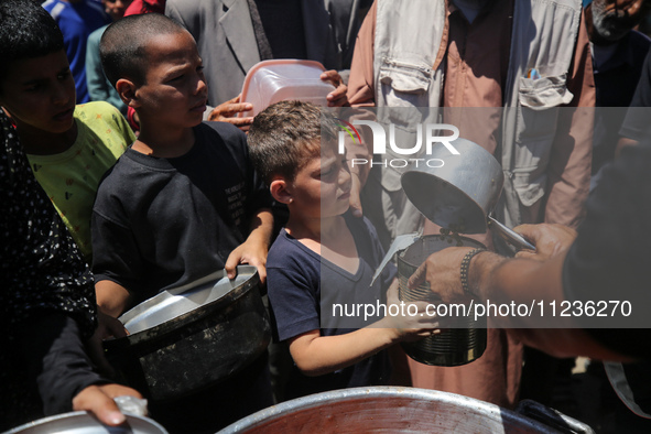 Displaced Palestinians are receiving food portions from a large pot at a public kitchen in Deir el-Balah in the central Gaza Strip on May 13...