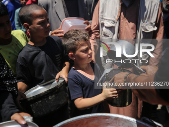 Displaced Palestinians are receiving food portions from a large pot at a public kitchen in Deir el-Balah in the central Gaza Strip on May 13...