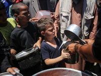 Displaced Palestinians are receiving food portions from a large pot at a public kitchen in Deir el-Balah in the central Gaza Strip on May 13...