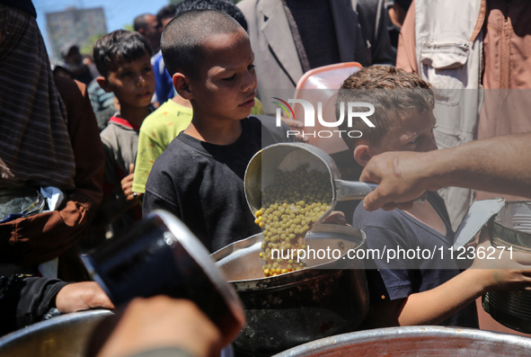 Displaced Palestinians are receiving food portions from a large pot at a public kitchen in Deir el-Balah in the central Gaza Strip on May 13...