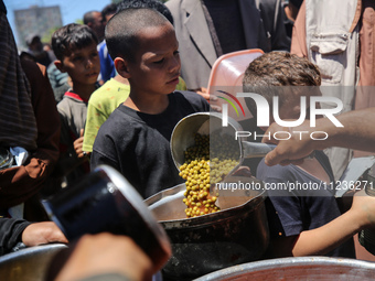 Displaced Palestinians are receiving food portions from a large pot at a public kitchen in Deir el-Balah in the central Gaza Strip on May 13...