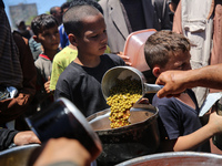 Displaced Palestinians are receiving food portions from a large pot at a public kitchen in Deir el-Balah in the central Gaza Strip on May 13...