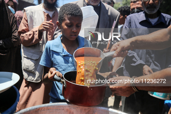 Displaced Palestinians are receiving food portions from a large pot at a public kitchen in Deir el-Balah in the central Gaza Strip on May 13...