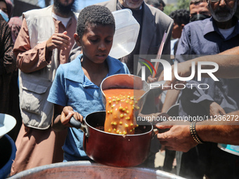 Displaced Palestinians are receiving food portions from a large pot at a public kitchen in Deir el-Balah in the central Gaza Strip on May 13...