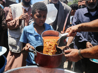 Displaced Palestinians are receiving food portions from a large pot at a public kitchen in Deir el-Balah in the central Gaza Strip on May 13...