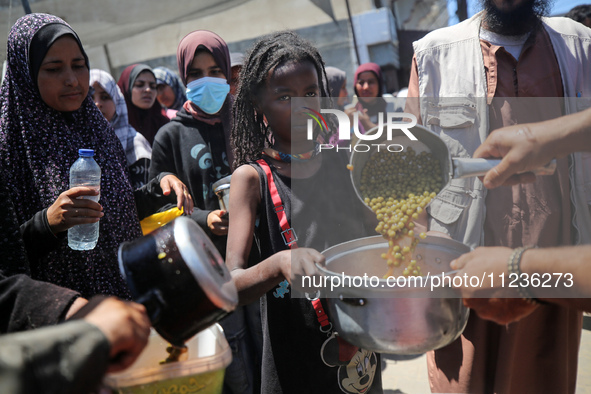 Displaced Palestinians are receiving food portions from a large pot at a public kitchen in Deir el-Balah in the central Gaza Strip on May 13...