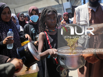 Displaced Palestinians are receiving food portions from a large pot at a public kitchen in Deir el-Balah in the central Gaza Strip on May 13...