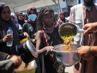 Displaced Palestinians are receiving food portions from a large pot at a public kitchen in Deir el-Balah in the central Gaza Strip on May 13...