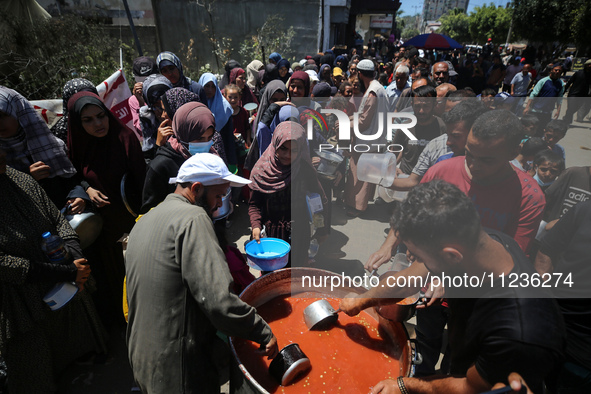 Displaced Palestinians are receiving food portions from a large pot at a public kitchen in Deir el-Balah in the central Gaza Strip on May 13...