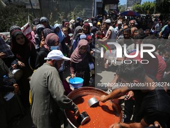 Displaced Palestinians are receiving food portions from a large pot at a public kitchen in Deir el-Balah in the central Gaza Strip on May 13...