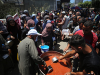 Displaced Palestinians are receiving food portions from a large pot at a public kitchen in Deir el-Balah in the central Gaza Strip on May 13...