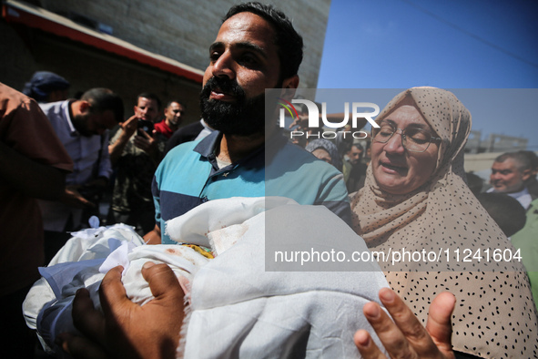 A man is carrying the shrouded body of a child, killed in an overnight Israeli strike on the Al-Breij refugee camp, during a mass funeral at...