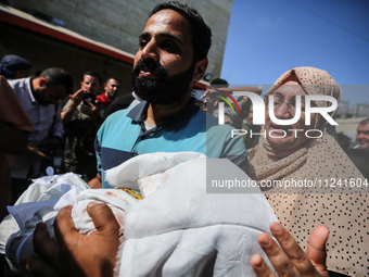 A man is carrying the shrouded body of a child, killed in an overnight Israeli strike on the Al-Breij refugee camp, during a mass funeral at...