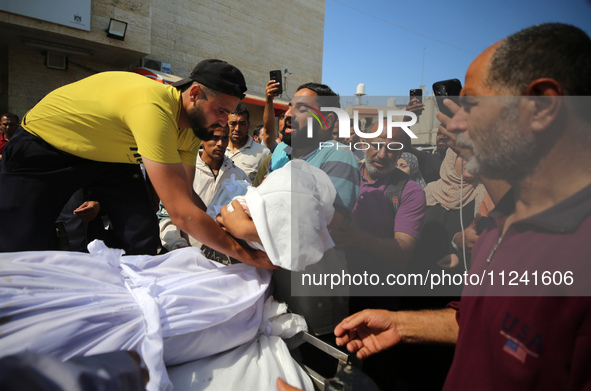 A man is carrying the shrouded body of a child, killed in an overnight Israeli strike on the Al-Breij refugee camp, during a mass funeral at...