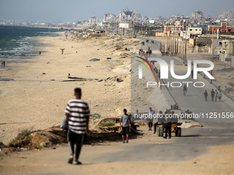 Palestinians are standing on a beach, as a U.S.-built pier is pictured in the background, as seen from central Gaza Strip, on May 18, 2024 (