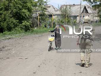 A serviceman is walking past an elderly woman who is pushing a bicycle along a street in Chasiv Yar, Donetsk region, eastern Ukraine, on May...