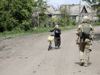 A serviceman is walking past an elderly woman who is pushing a bicycle along a street in Chasiv Yar, Donetsk region, eastern Ukraine, on May...