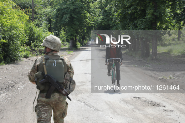 A serviceman is walking past an elderly man riding a bicycle along a street in Chasiv Yar, Donetsk region, eastern Ukraine, on May 18, 2024....