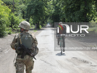 A serviceman is walking past an elderly man riding a bicycle along a street in Chasiv Yar, Donetsk region, eastern Ukraine, on May 18, 2024....