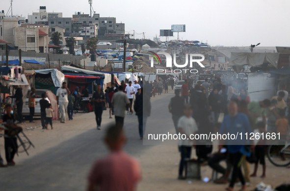 Palestinians are walking amidst tents housing internally displaced people, along the coastline in Deir el-Balah in the central Gaza Strip, o...