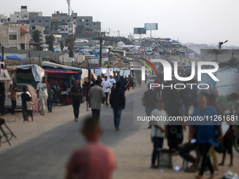 Palestinians are walking amidst tents housing internally displaced people, along the coastline in Deir el-Balah in the central Gaza Strip, o...