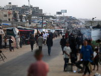 Palestinians are walking amidst tents housing internally displaced people, along the coastline in Deir el-Balah in the central Gaza Strip, o...