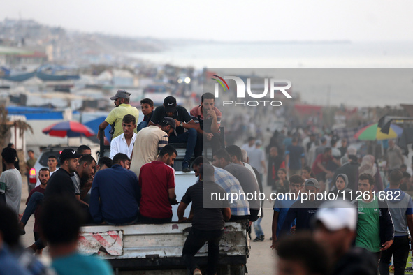 Palestinians are walking amidst tents housing internally displaced people, along the coastline in Deir el-Balah in the central Gaza Strip, o...