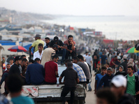 Palestinians are walking amidst tents housing internally displaced people, along the coastline in Deir el-Balah in the central Gaza Strip, o...