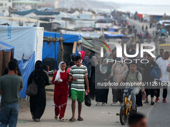 Palestinians are walking amidst tents housing internally displaced people, along the coastline in Deir el-Balah in the central Gaza Strip, o...