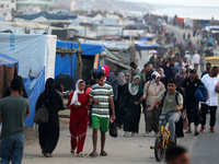 Palestinians are walking amidst tents housing internally displaced people, along the coastline in Deir el-Balah in the central Gaza Strip, o...