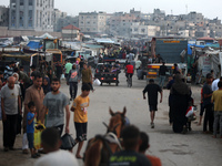 Palestinians are walking amidst tents housing internally displaced people, along the coastline in Deir el-Balah in the central Gaza Strip, o...