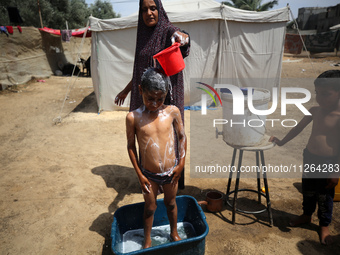 A displaced Palestinian mother is showering her child amid a heat wave outside a tent at a temporary camp in Deir el-Balah in the central Ga...