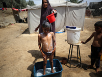 A displaced Palestinian mother is showering her child amid a heat wave outside a tent at a temporary camp in Deir el-Balah in the central Ga...