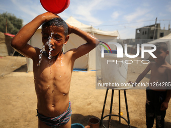 A displaced Palestinian mother is showering her child amid a heat wave outside a tent at a temporary camp in Deir el-Balah in the central Ga...