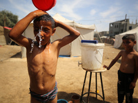 A displaced Palestinian mother is showering her child amid a heat wave outside a tent at a temporary camp in Deir el-Balah in the central Ga...