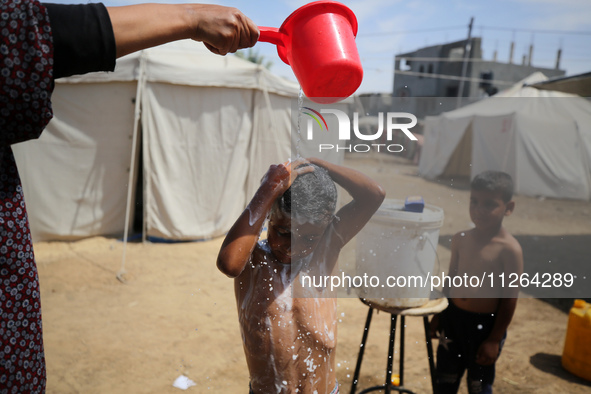 A displaced Palestinian mother is showering her child amid a heat wave outside a tent at a temporary camp in Deir el-Balah in the central Ga...