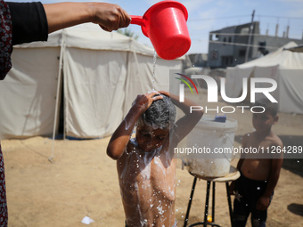 A displaced Palestinian mother is showering her child amid a heat wave outside a tent at a temporary camp in Deir el-Balah in the central Ga...