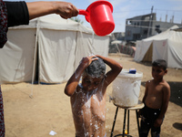 A displaced Palestinian mother is showering her child amid a heat wave outside a tent at a temporary camp in Deir el-Balah in the central Ga...