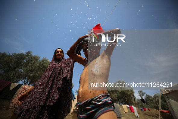 A displaced Palestinian mother is showering her child amid a heat wave outside a tent at a temporary camp in Deir el-Balah in the central Ga...