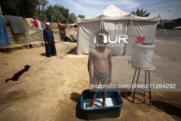 A displaced Palestinian mother is showering her child amid a heat wave outside a tent at a temporary camp in Deir el-Balah in the central Ga...