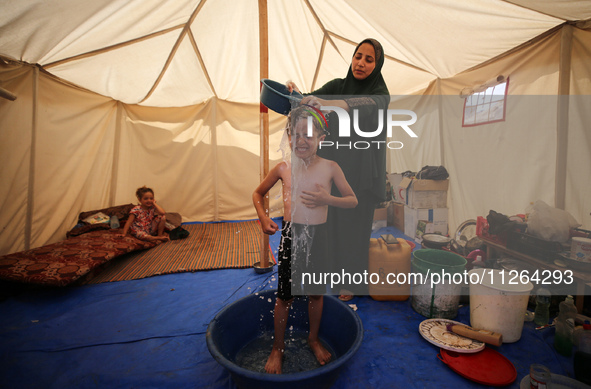 A displaced Palestinian mother is showering her child amid a heat wave inside a tent at a temporary camp in Deir el-Balah in the central Gaz...