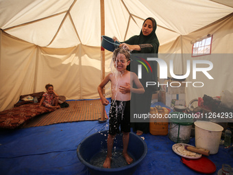 A displaced Palestinian mother is showering her child amid a heat wave inside a tent at a temporary camp in Deir el-Balah in the central Gaz...