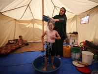 A displaced Palestinian mother is showering her child amid a heat wave inside a tent at a temporary camp in Deir el-Balah in the central Gaz...