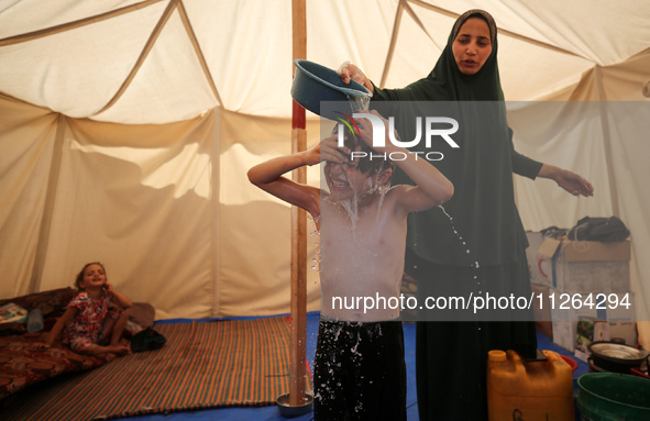 A displaced Palestinian mother is showering her child amid a heat wave inside a tent at a temporary camp in Deir el-Balah in the central Gaz...